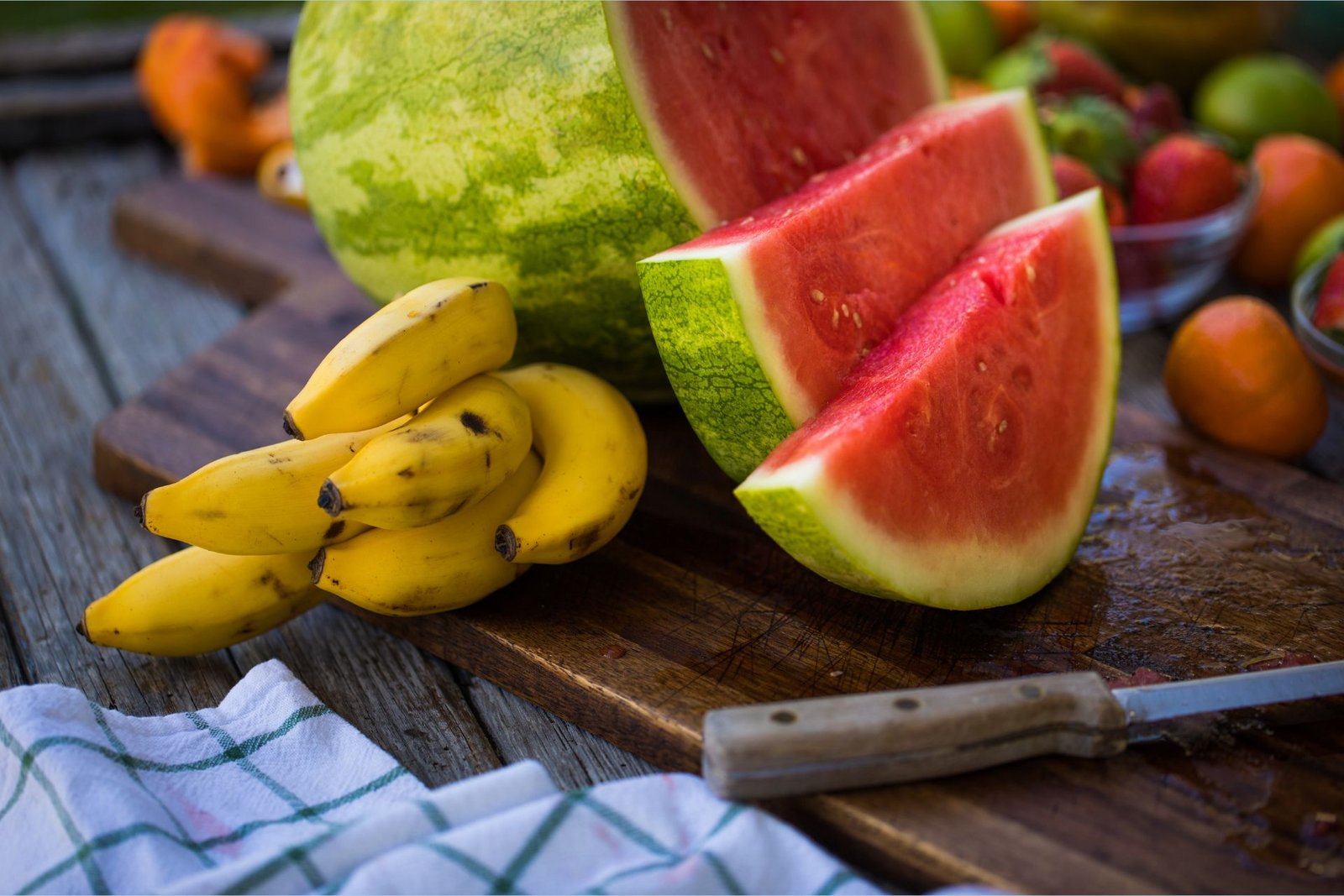 Bananele bogate în potasiu se află alături de un pepene verde feliat bogat în L-citrulină pe o planșă de tocat